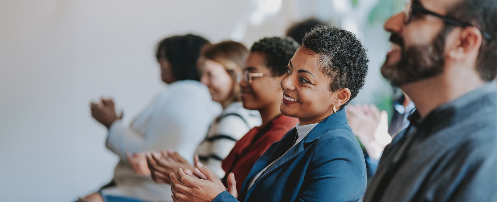 A group of people seated in a row, clapping during an event.