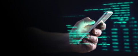 A person holding a phone with visible computer code on the display.