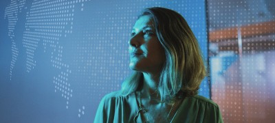 A woman stands in front of a large screen displaying a colorful world map.