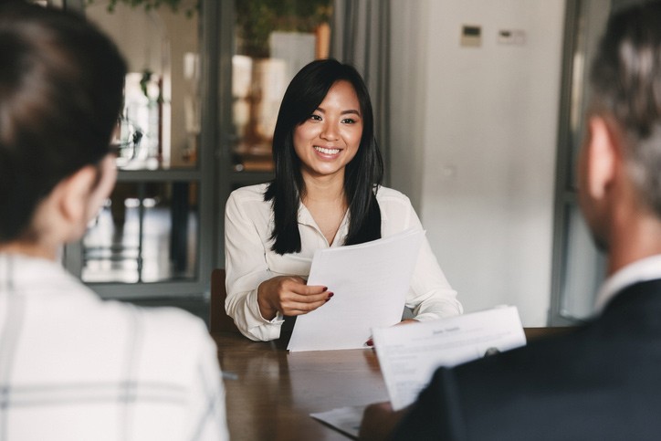 Young woman smiling and holding resume while interviewing as candidate for job